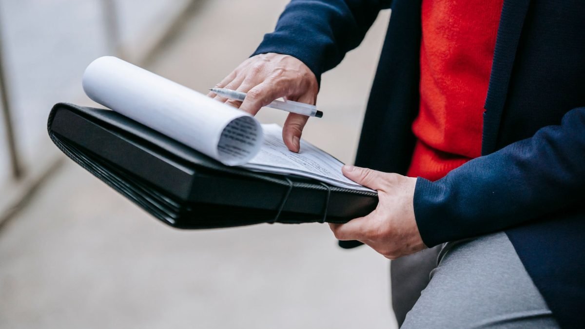 Close-up of a professional person reviewing documents outdoors. Engaged in work with focus on writing materials. — Discoverin