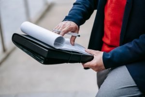 Close-up of a professional person reviewing documents outdoors. Engaged in work with focus on writing materials. — Discoverin