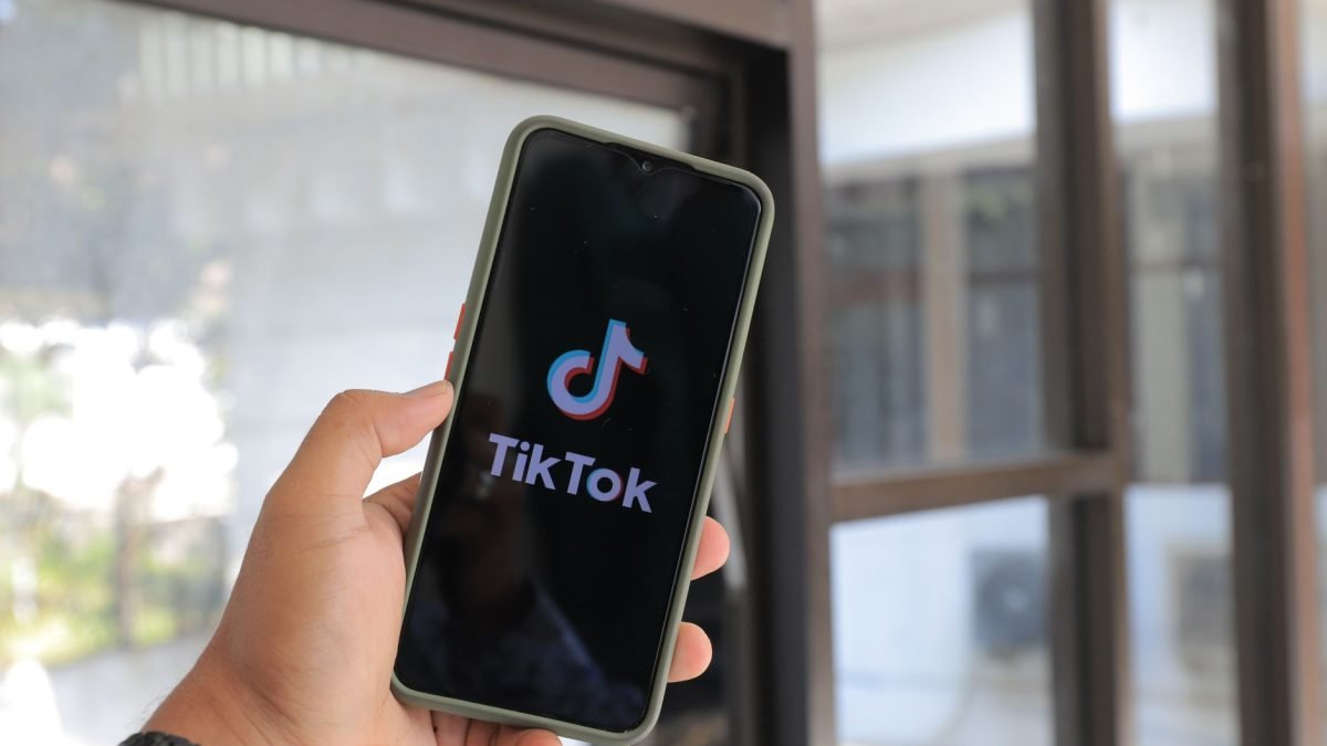 Close-up of a hand holding a smartphone displaying the TikTok app indoors. — Gain Access to Advanced Facebook Ads Tools throu