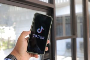 Close-up of a hand holding a smartphone displaying the TikTok app indoors. — Gain Access to Advanced Facebook Ads Tools throu