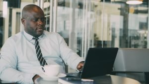 Focused businessman uses laptop in stylish cafe, sipping coffee. Perfect for business or lifestyle themes. — Joseph Samuels I
