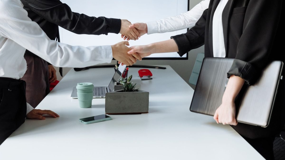 Professionals sealing a deal with a handshake across a conference table during a business meeting. — Revolutionizing Recovery