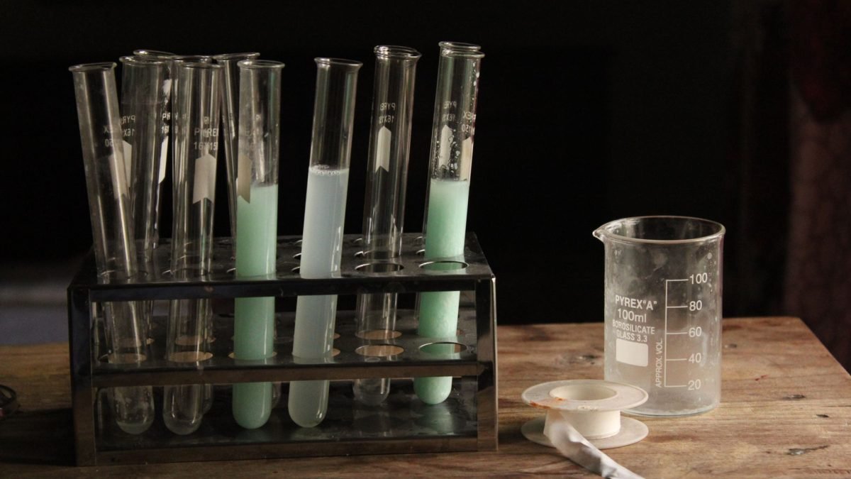 Test tubes and beaker with colorful chemicals on a wooden table in a dim lab. — test