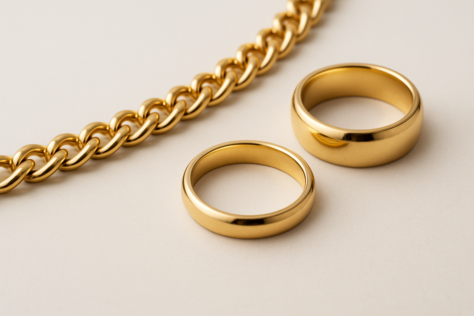 Close-up of gold jewelry including a chain and two rings on a neutral background